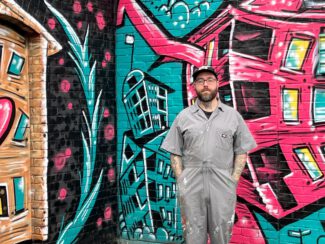 Artist Eamon Gillen stands in front of his mural painted on the Hotel Vernon building in Kelley Square (Photo by Kiernan Dunlop)