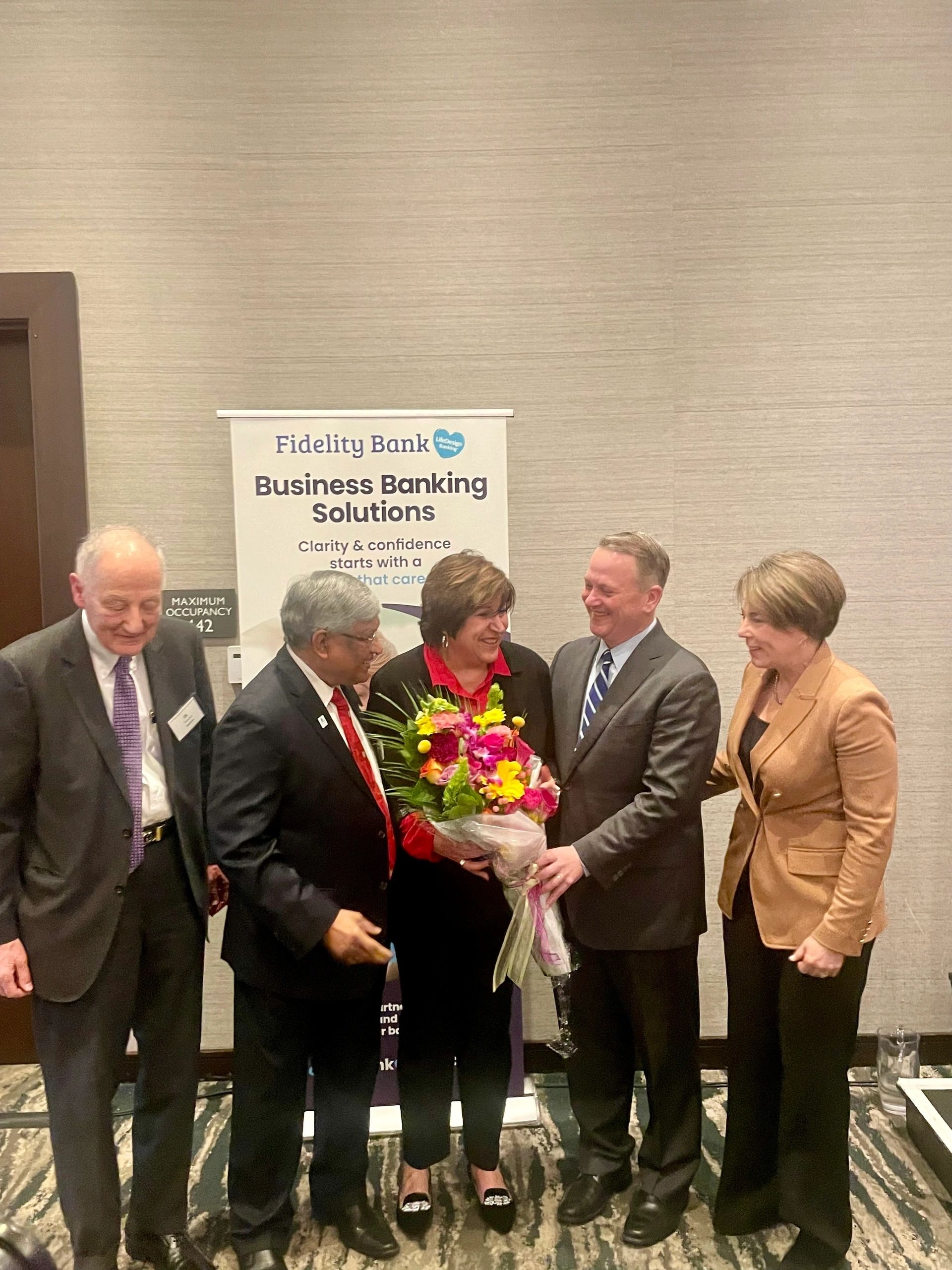 Linda Salem Pervier receives flowers from Timothy Murray after the chamber announced the Linda Salem Permanent Restricted Fund in her honor. Governor Maura Healey is to the right. Chamber board of directors chair Dr. Satya Mitra is second from left and D. Moschos, board chair of the Worcester Regional Strategic Opportunities Foundation is to the far left (photo by Bill Doyle)