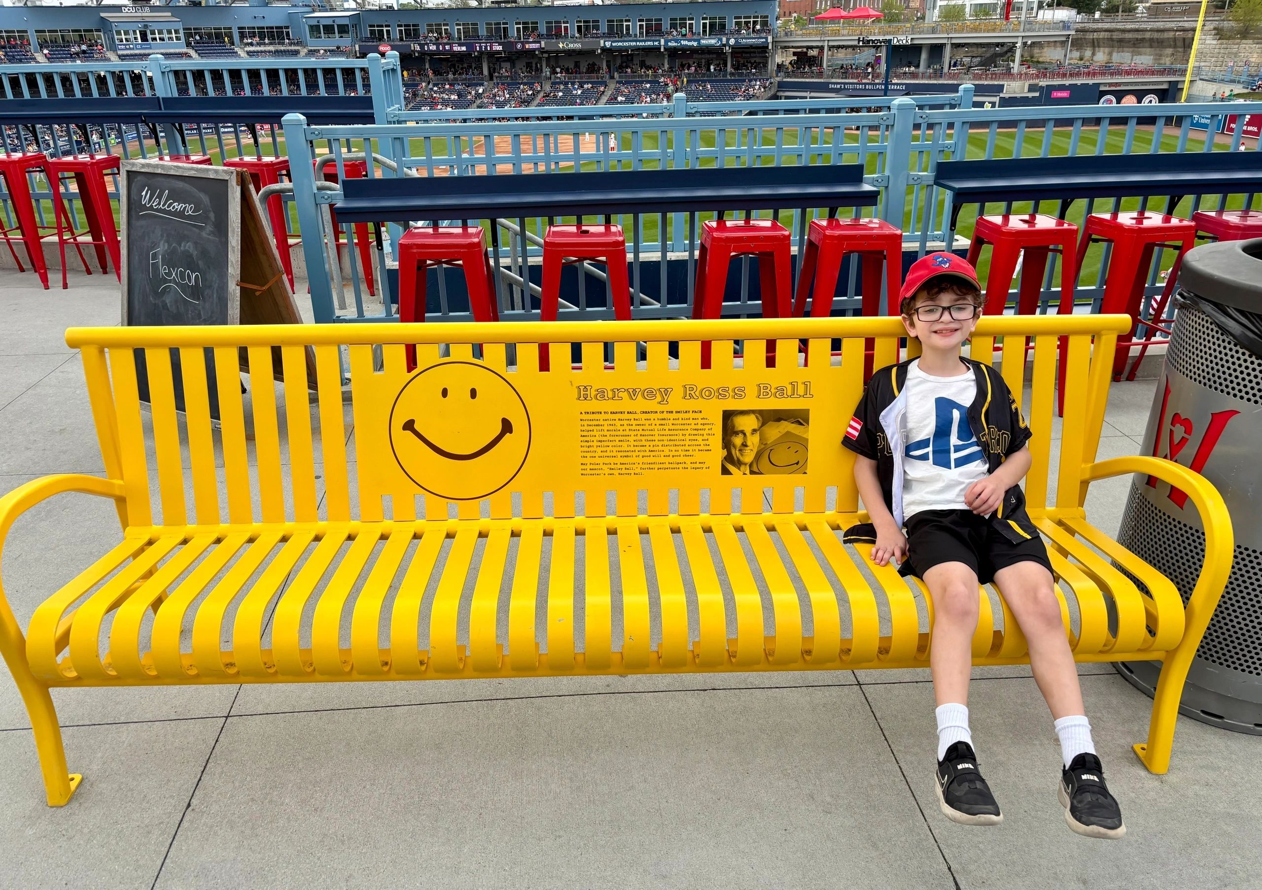 Rafa Melendez, 8, of Worcester is a big fan of Smiley Ball and he’s shown here sitting on the Harvey Ball bench at Polar Park (photo by Bill Doyle)