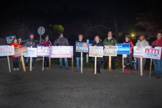 A large group of campaigners show their signs to cars entering the Congregation Beth Israel voting location (photo by Steve Smith)