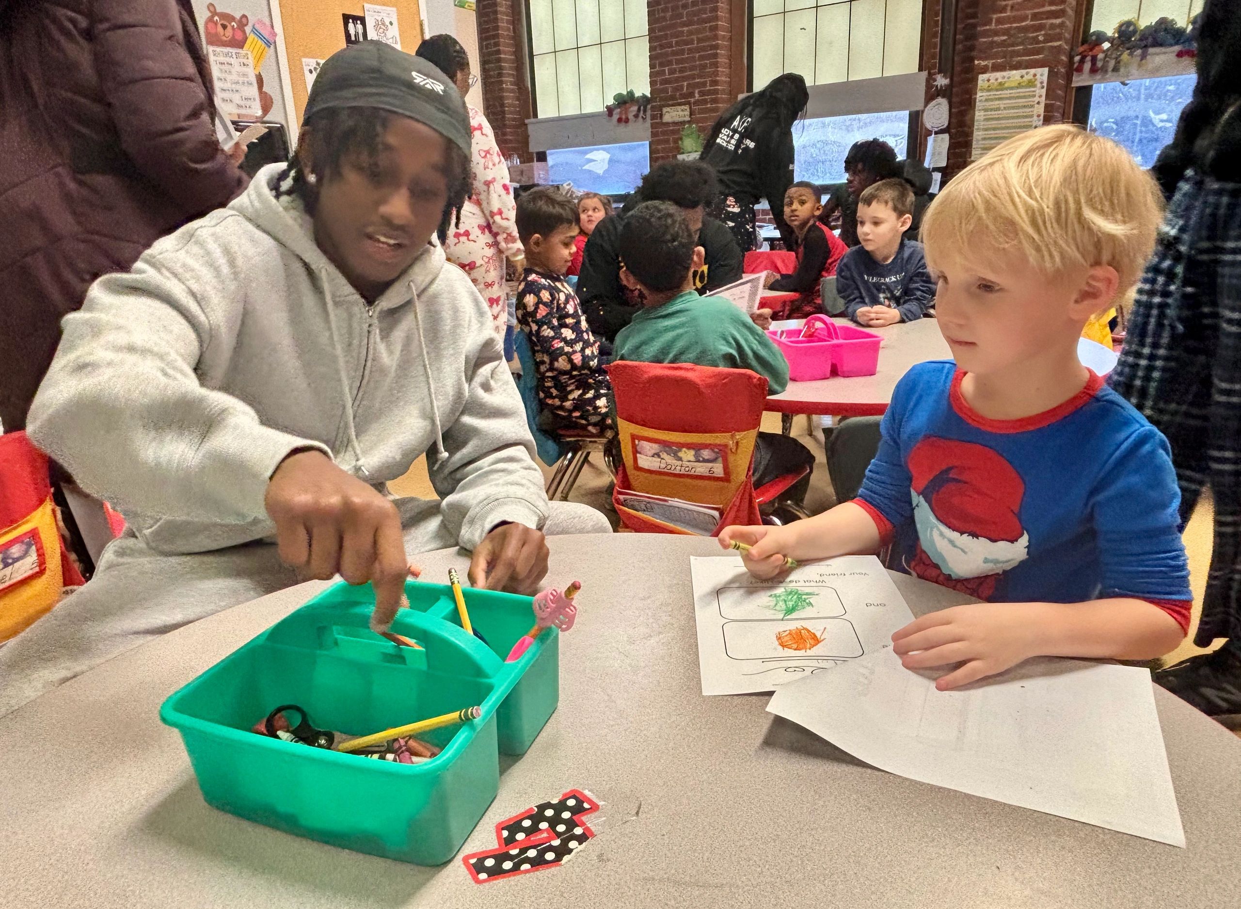Senior John Paul Waweru colors with kindergartner Hayden Guitar at the Abby Kelley Foster Charter Public School (photo by Bill Doyle)